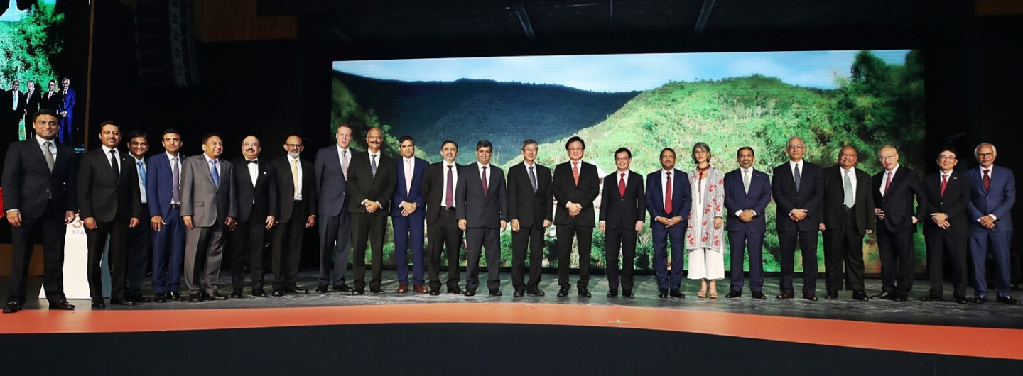 Group of people in suits standing on a stage in front of a landscape backdrop.